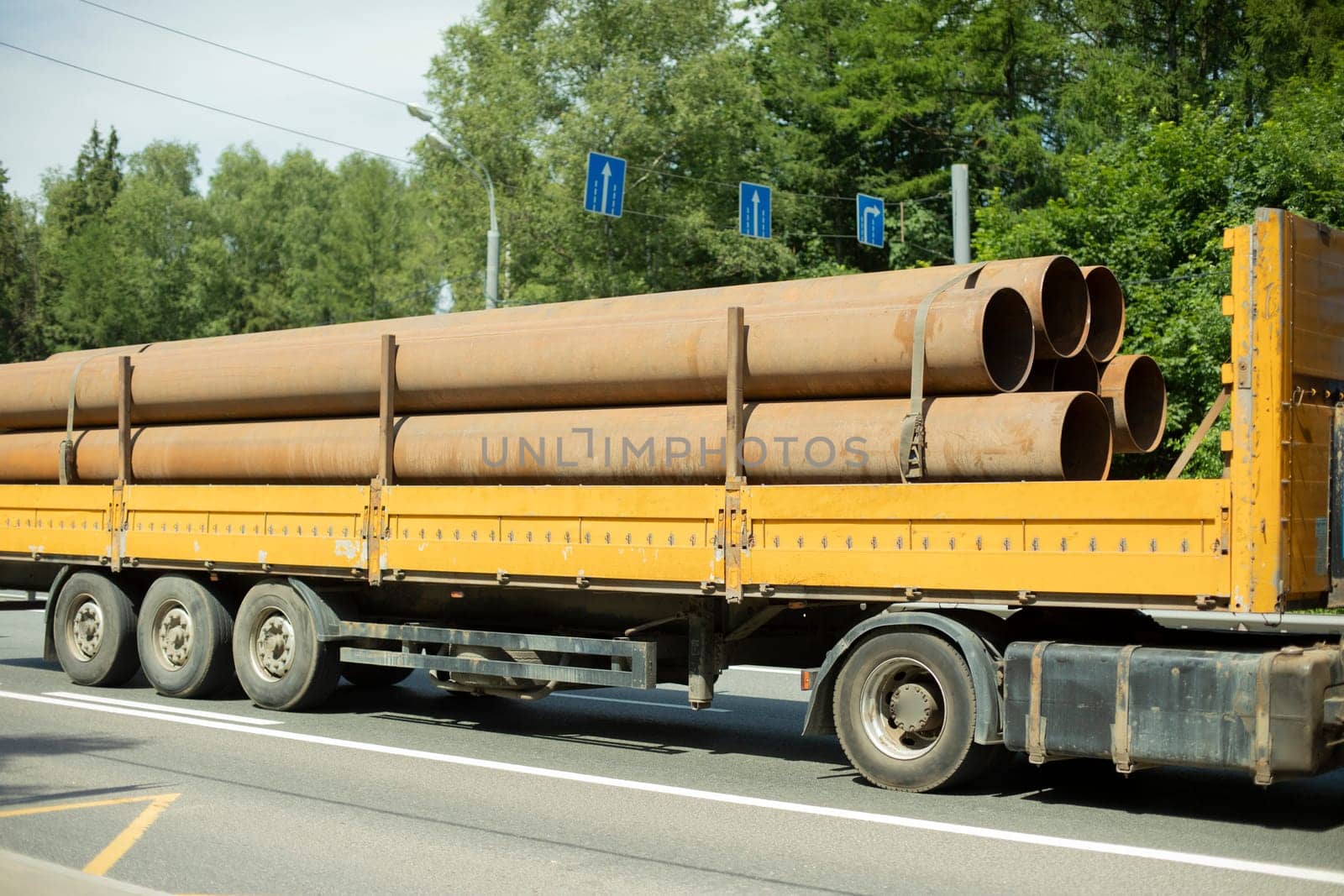 Transportation of pipes on truck trailer. Steel pipes on truck. Transportation by highway. Yellow trailer for industrial purposes.
