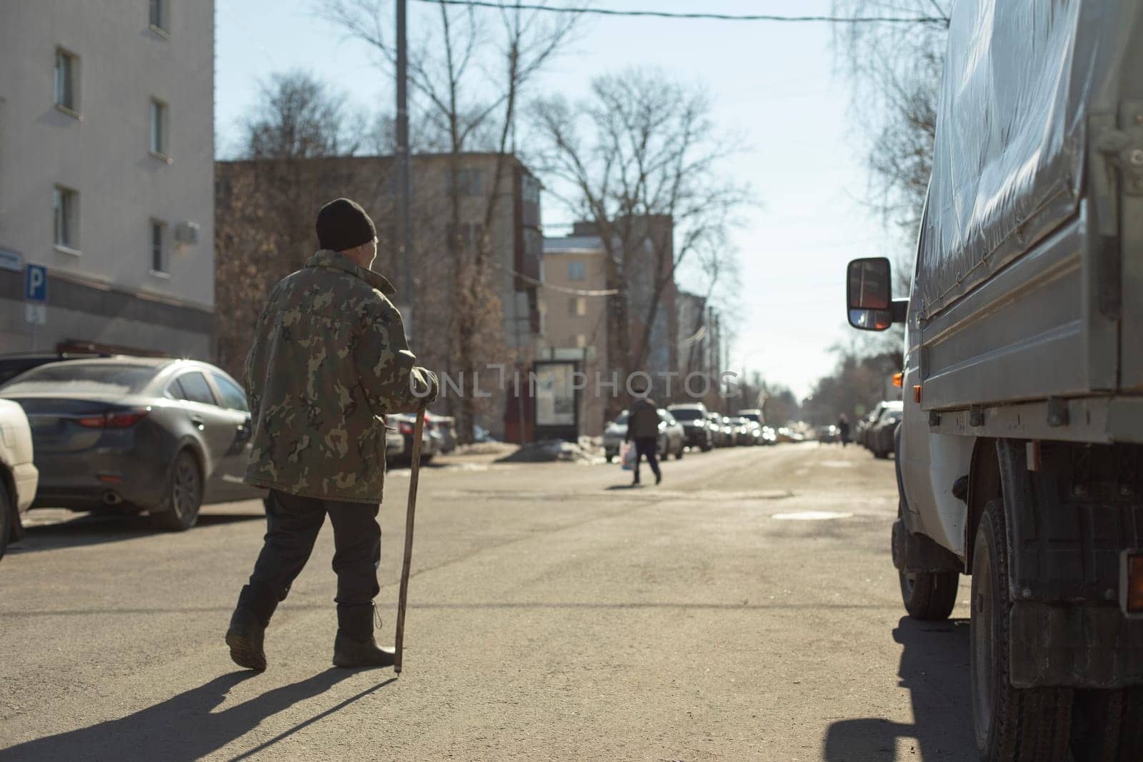 Grandpa walks through square. Elderly man in town. Man with stick. Pensioner on street. by OlegKopyov