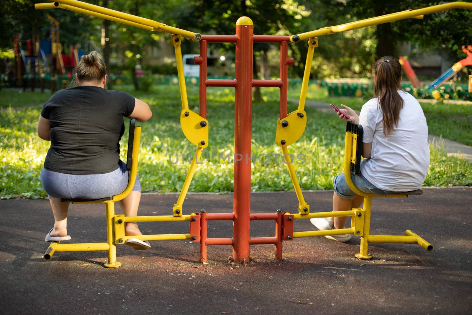 Girls on sports field. Women in training. Outdoor fitness. Lazy people. Exercise machine for muscle training in yard of house.