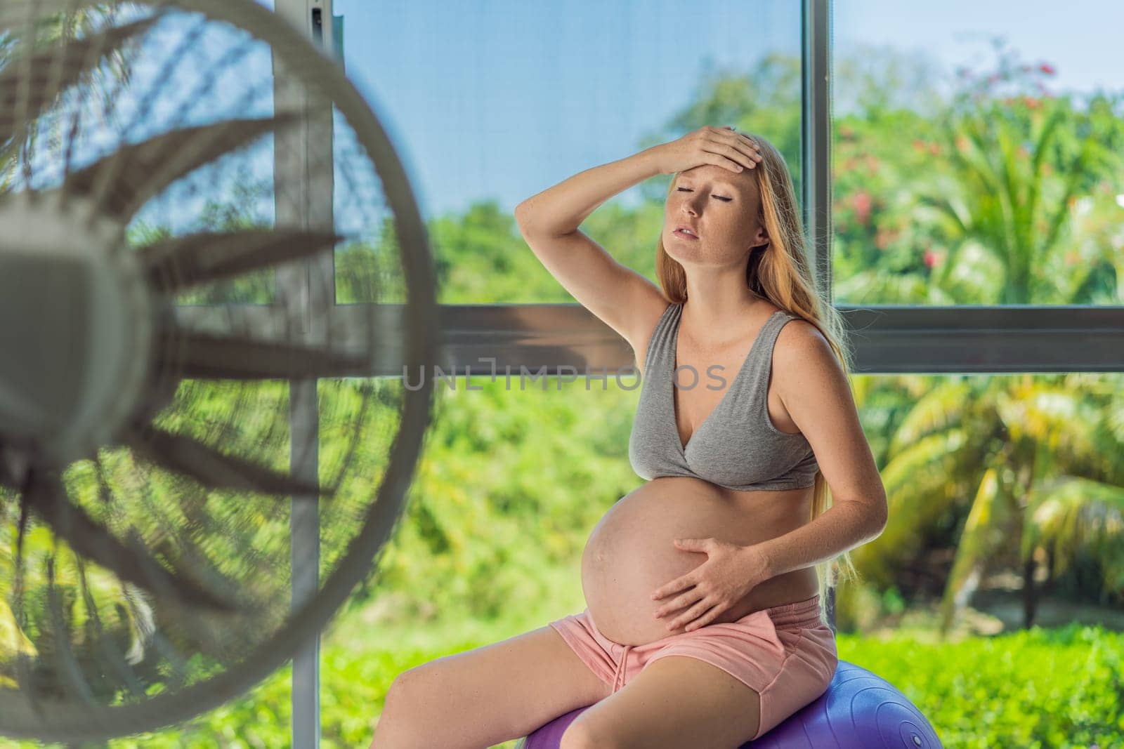 A pregnant woman seeks relief from an abnormal heatwave by using a fan, ensuring her comfort and well-being during sweltering conditions.