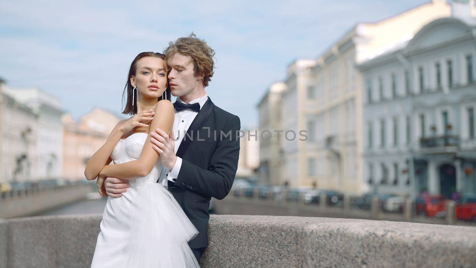 Newlyweds hug on European street. Action. Stylish couple of newlyweds embrace on background of European buildings. Beautiful newlyweds on street in summer.