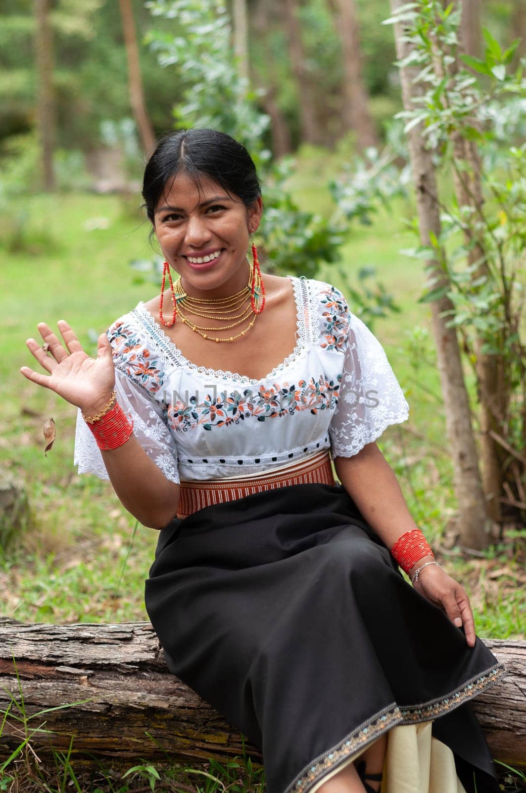 sweet indigenous woman from ecuador sitting on a fallen tree in a forest smiling and waving to the camera. by Raulmartin