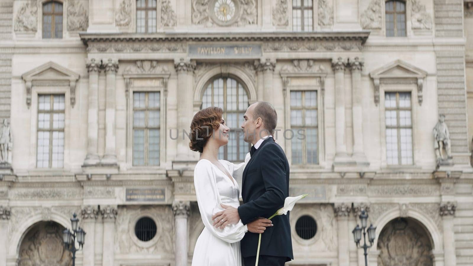 Adult couple in elegant outfits hugging. Action. Luxurious couple embraces in love on background of palace. Couple in love in elegant outfits on old square.