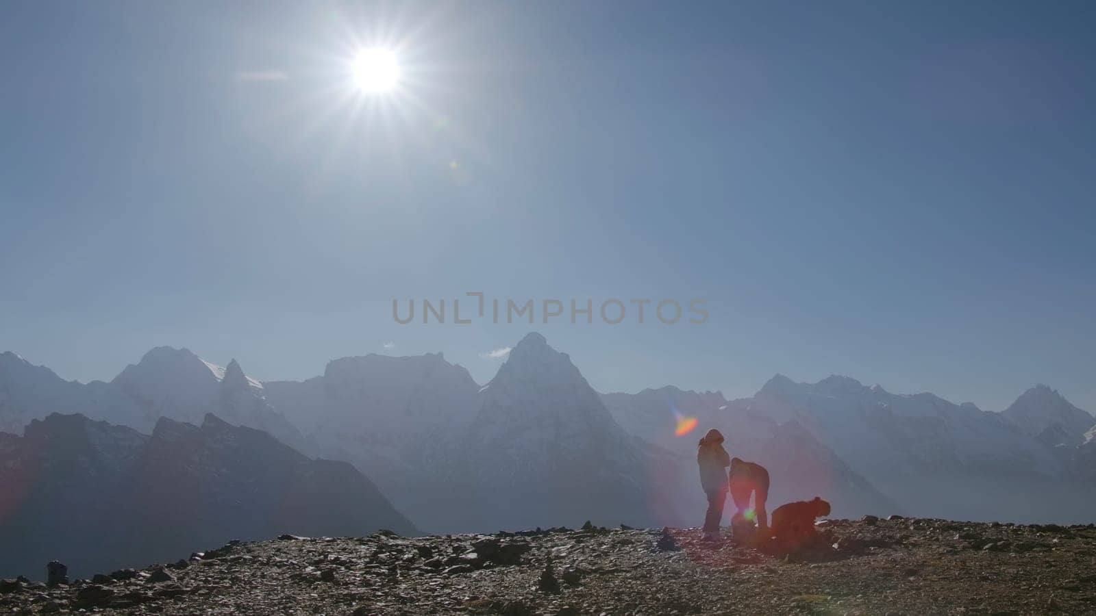 Tourists on background of mountain landscape with bright sun. Creative. Beautiful motivating view of peaks of snowy mountains in rays of sun. Hikers on background of mountain peaks on sunny day by Mediawhalestock