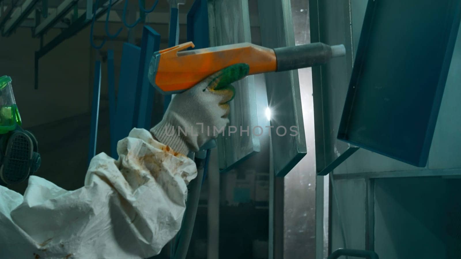 A worker coats a metal part with a powder coating using a spray gun. Creative. Powder coating of metal products, factory powder coating of metal structures