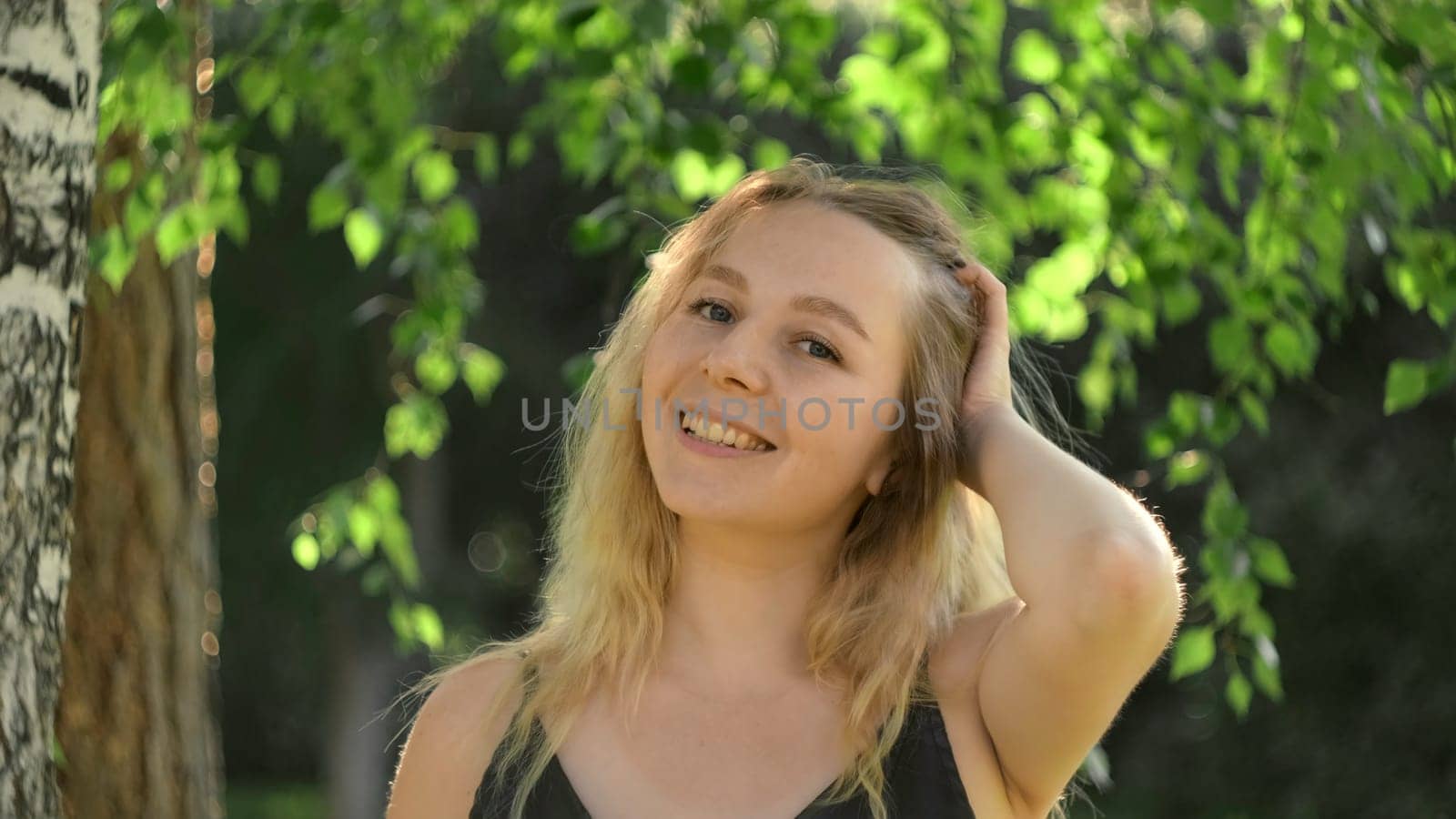 Beautiful young woman on birch background in summer. Concept. Bright attractive woman by birch tree on sunny summer day. Beautiful woman with blonde hair smiles in park in summer by Mediawhalestock