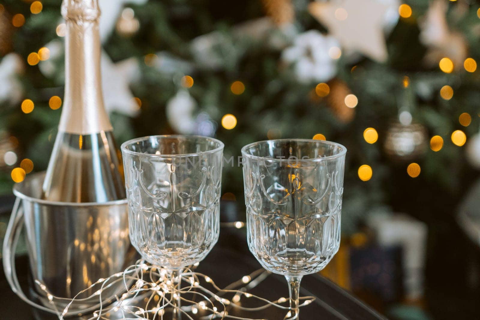 Champagne glasses, New Year decor. New Year's festive setting, family holidays.Two glasses of champagne are on the table against the background of New Year's decorated tree. by Matiunina