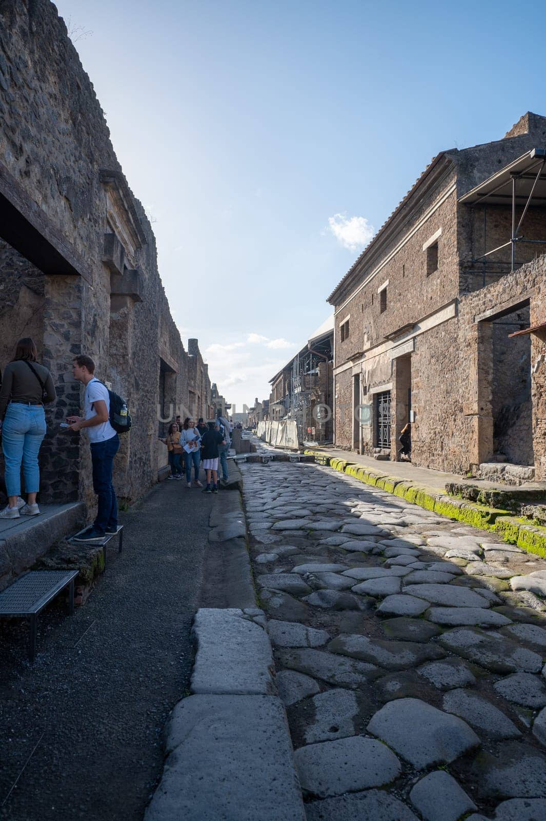 Pompeii, Italy : 2023 November 16 : People walking through the Ancient Pompeii (UNESCO World Heritage Site). Paving stones of Via del Foro in November 2023.