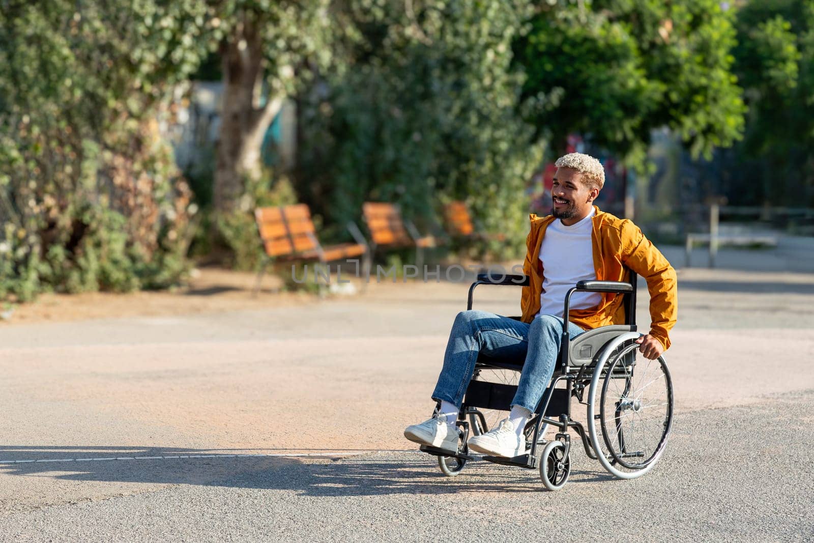 Young African American man sitting on a wheelchair outdoors in park. by Hoverstock