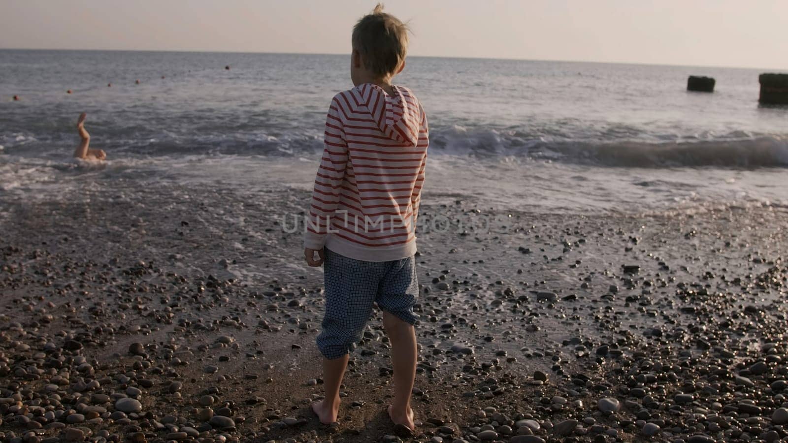 Rear view of a boy on pebble beach on a summer day. Creative. Concept of vacation