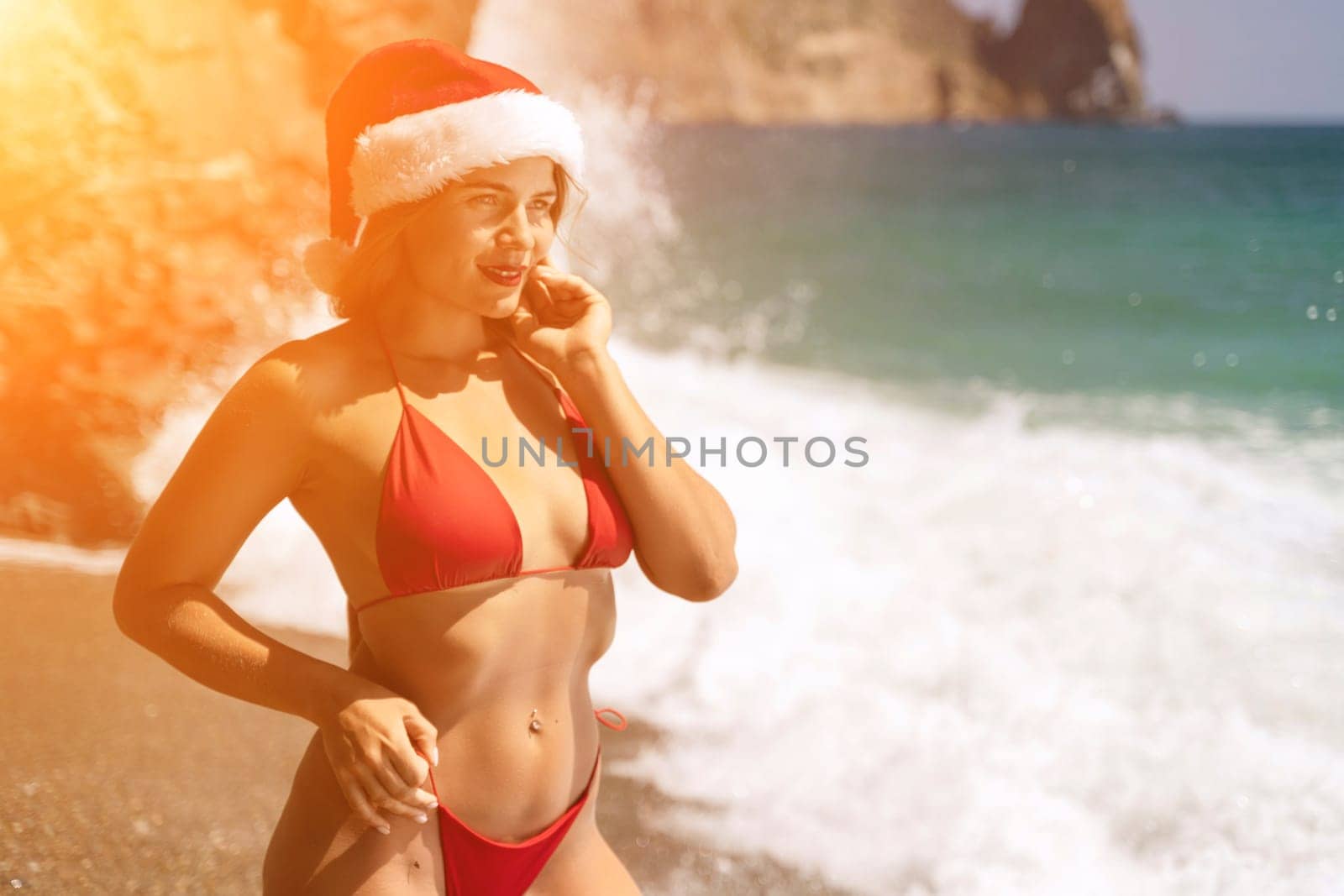 A woman in Santa hat on the seashore, dressed in a red swimsuit. New Year's celebration in a hot country