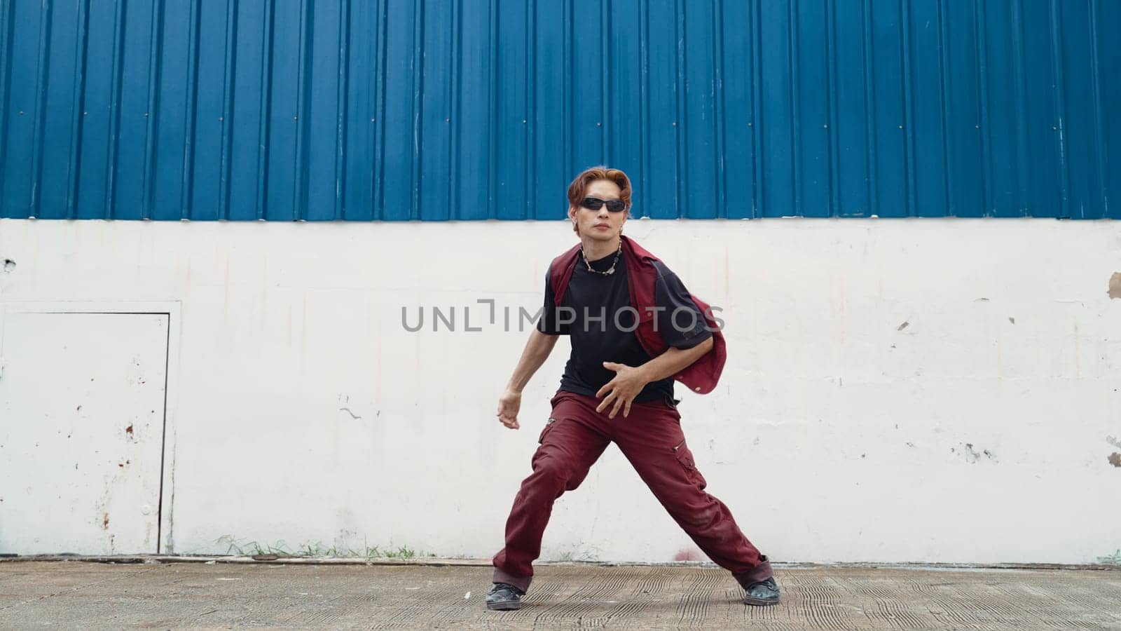 Handsome street dancer practicing break dancing at white back ground. Sport man wearing hip hop style while moving footsteps to music at street with blue background. Outdoor sport 2024. Endeavor.