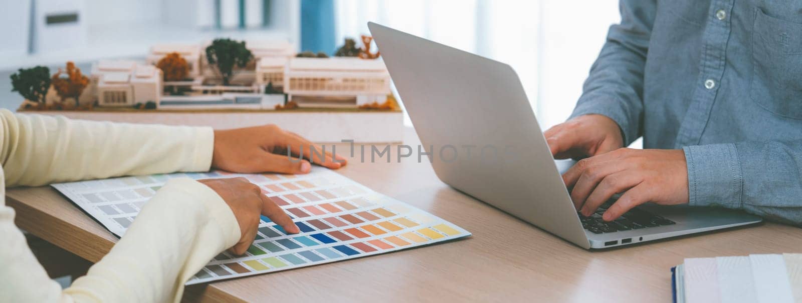Architect interior designer selects color by using color swatches during his colleague searching information by using laptop. Creative design and teamwork concept. Closeup. Variegated.