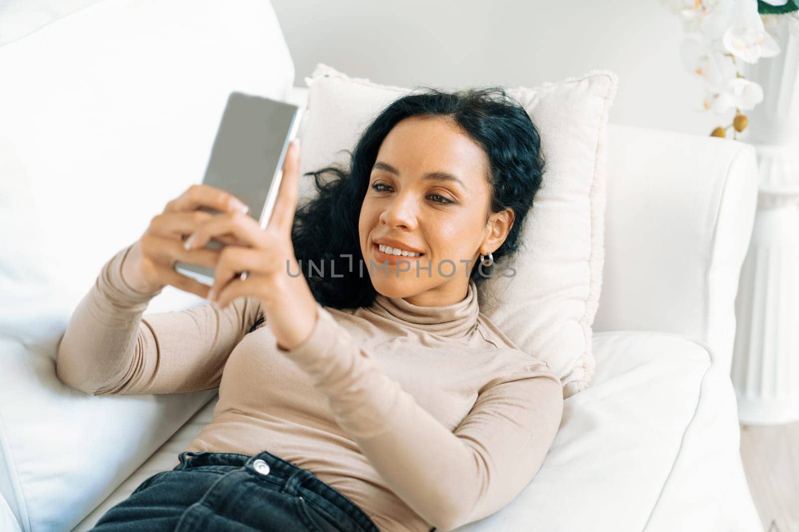 Relaxed young African American woman using crucial mobile phone on sofa couch in living room at home