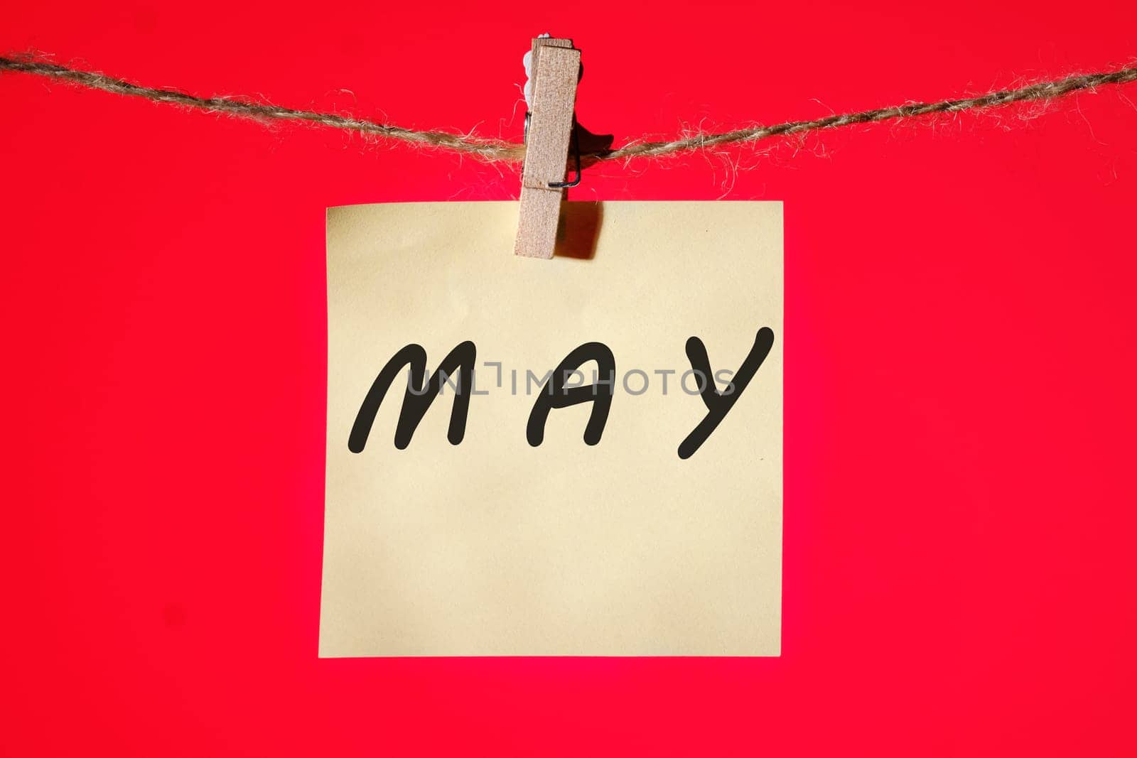 MAY text on a yellow sticker hanging on a rope with clothespins on a red background