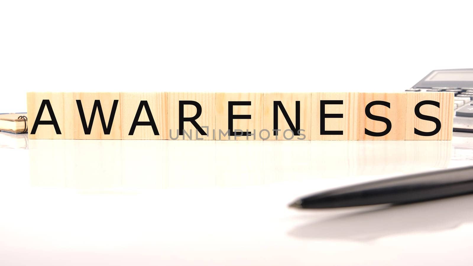 AWARENESS word word assembled from wooden cubes next to a calculator, pen and notepad