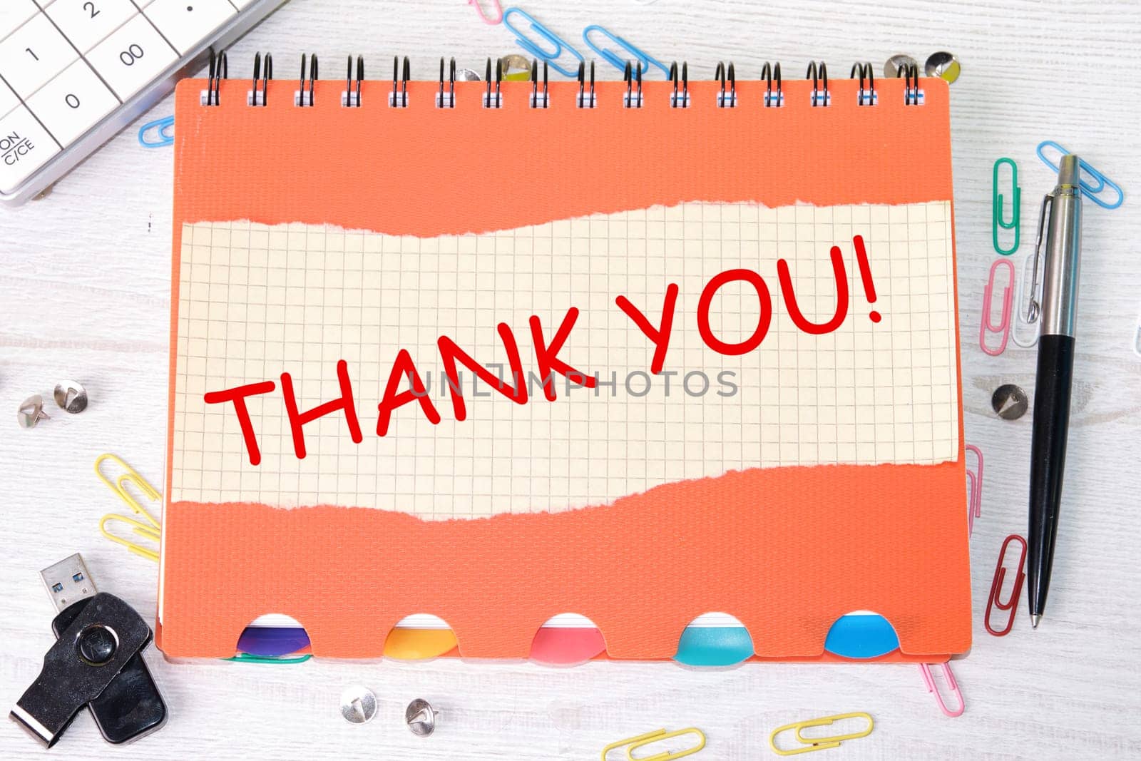 Thank you word is written on a sheet in a cage lying on a notebook on the table next to stationery