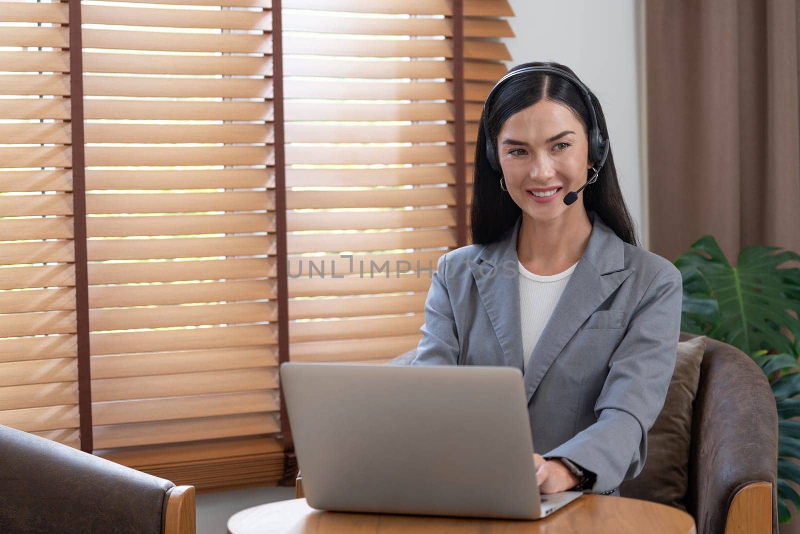 Female call center operator or customer service helpdesk staff working on workspace while talking on the headset to provide assistance for customer. Professional modern business service. Blithe