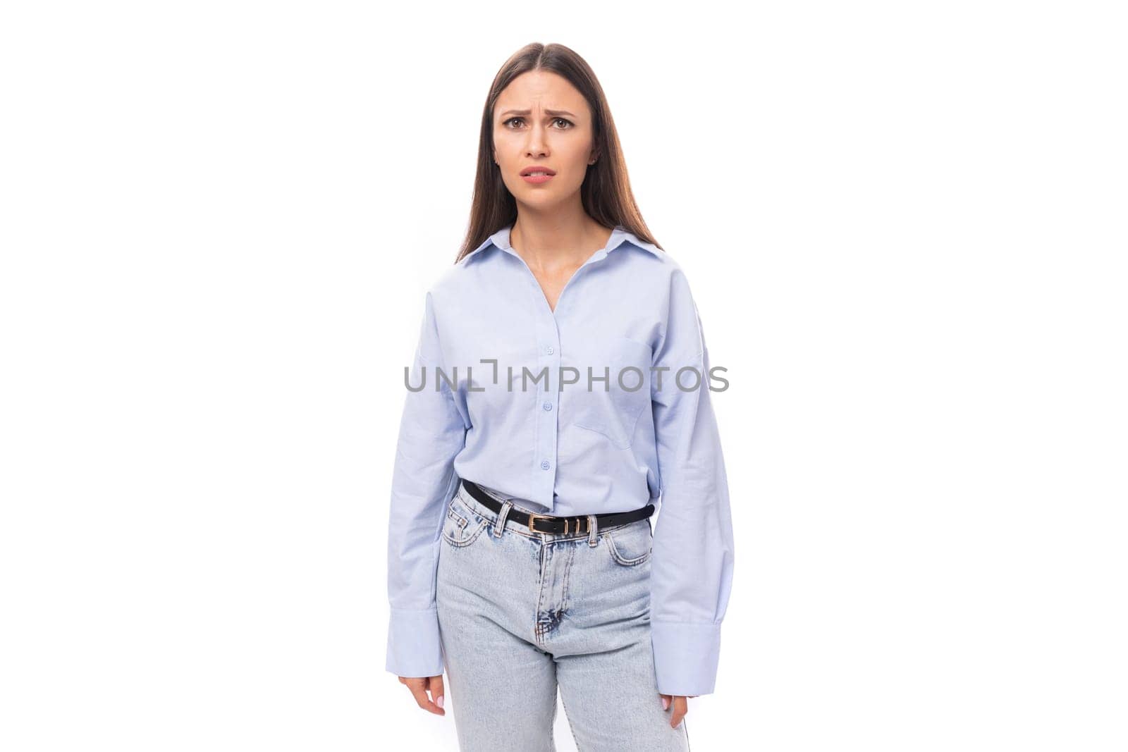 young caucasian model woman with dark straight hair dressed in a blue blouse looks upset at the camera.