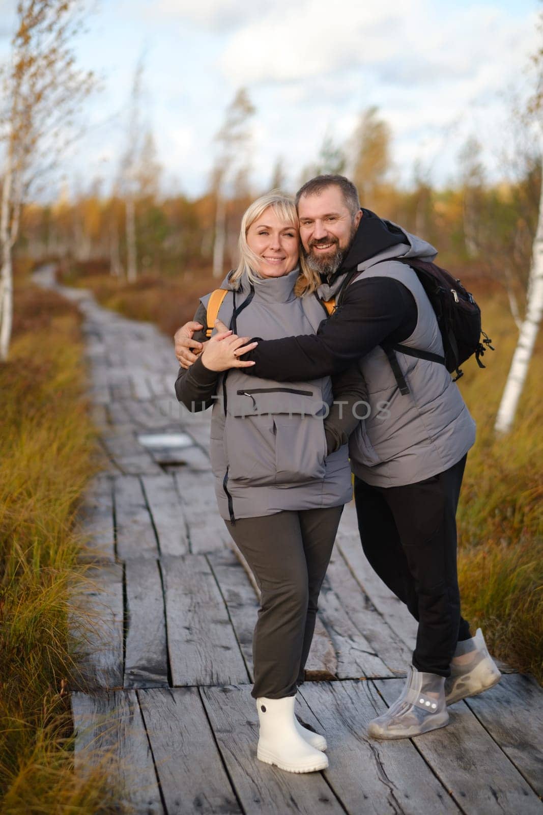 People in boots stand hugging on a wooden path in a swamp in Yelnya, Belarus.