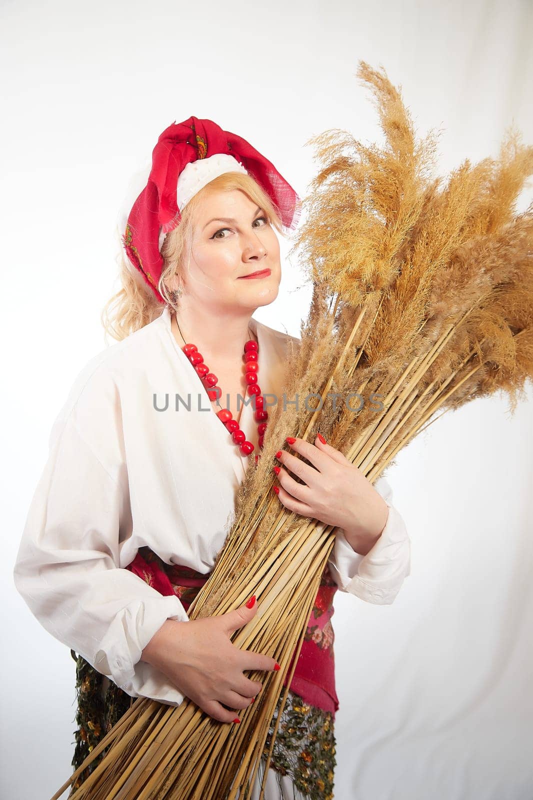 Portrait of heerful funny adult mature woman solokha with sheaf of ears. Female model in clothes of national ethnic Slavic style. Stylized Ukrainian, Belarusian or Russian woman in comic photo shoot by keleny