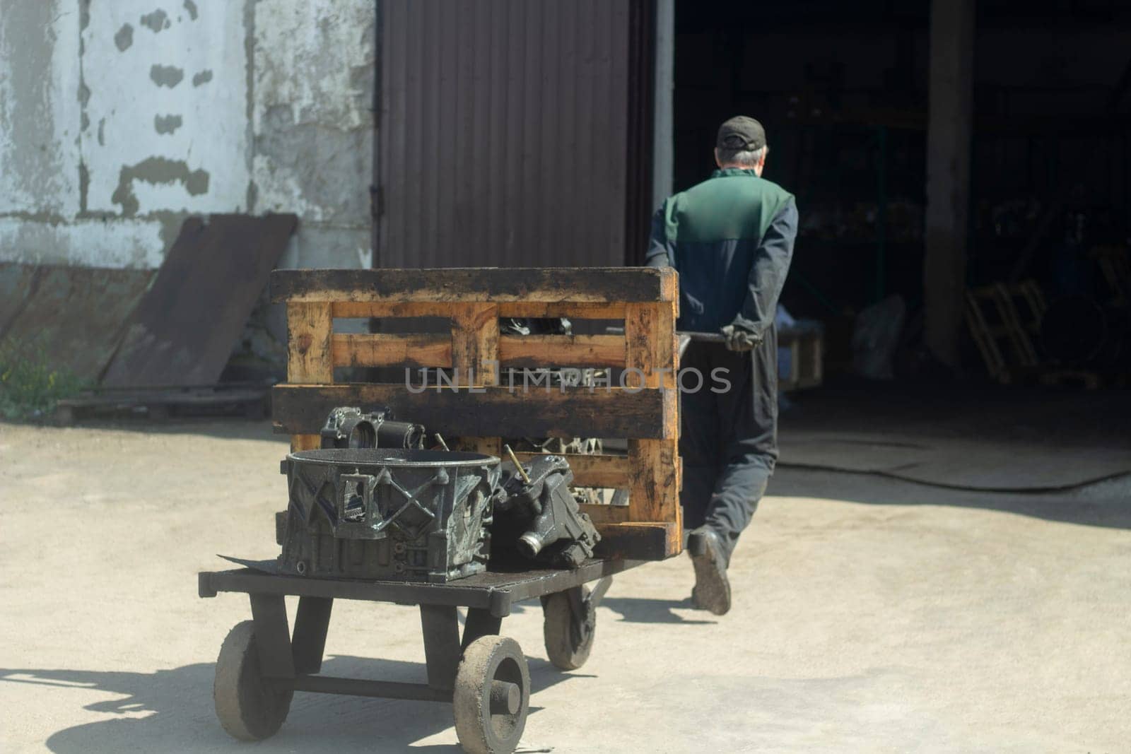 Man carries cart. Worker pulls load. Forklift on street. Man drags vehicle.