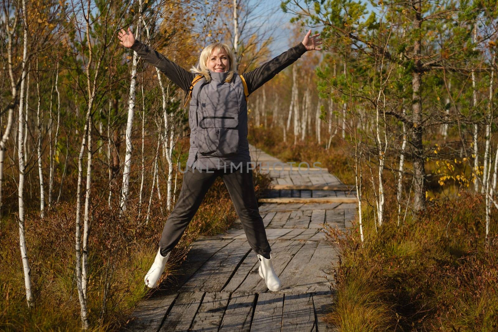 A happy woman with a backpack jumps on a wooden path in a swamp in Yelnya, Belarus by Lobachad