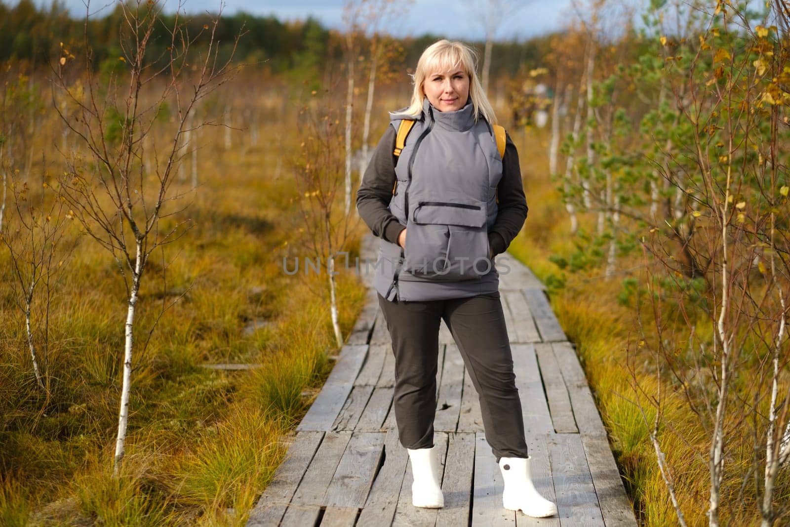 A woman stands on a wooden path in a swamp in Yelnya, Belarus by Lobachad