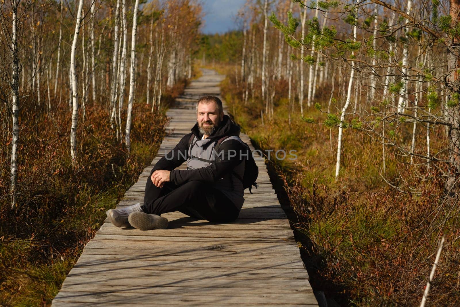 A man sits on a wooden path in a swamp in Yelnya, Belarus.