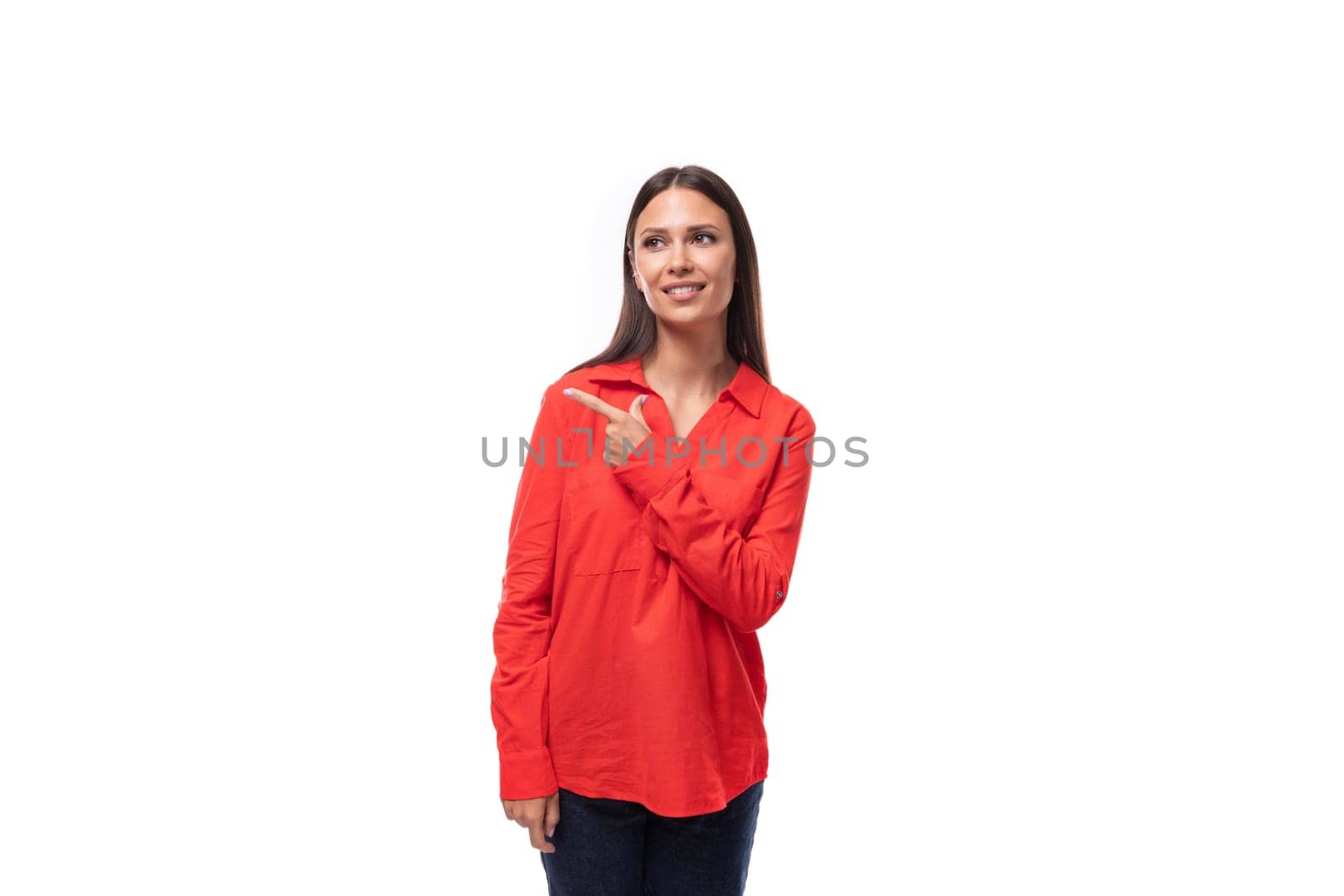 young brunette caucasian model woman dressed in a fashionable red shirt points with her hand to the space for advertising on a white background by TRMK