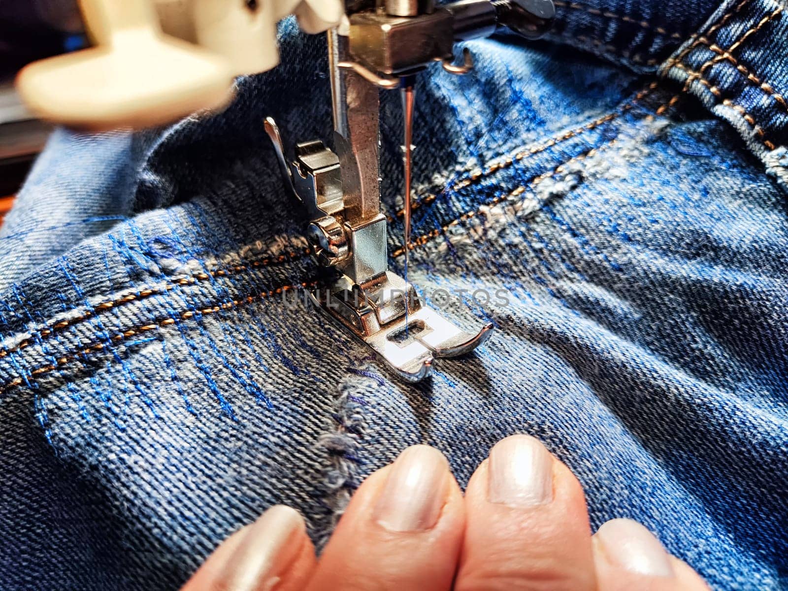 Sewing machine and blue jeans fabric. A woman's hand and fingers next to a sewing machine needle when sewing up a tear in denim by keleny