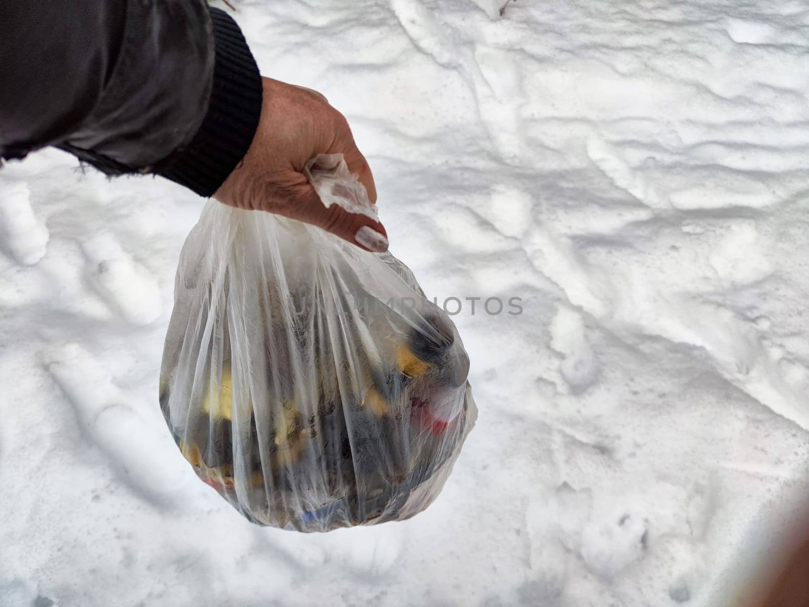 Bag of garbage in hand of woman and snow in forest on the background. A girl cleans up the trash after a picnic. A tourist is going to throw garbage in nature. The concept of environmental pollution by keleny