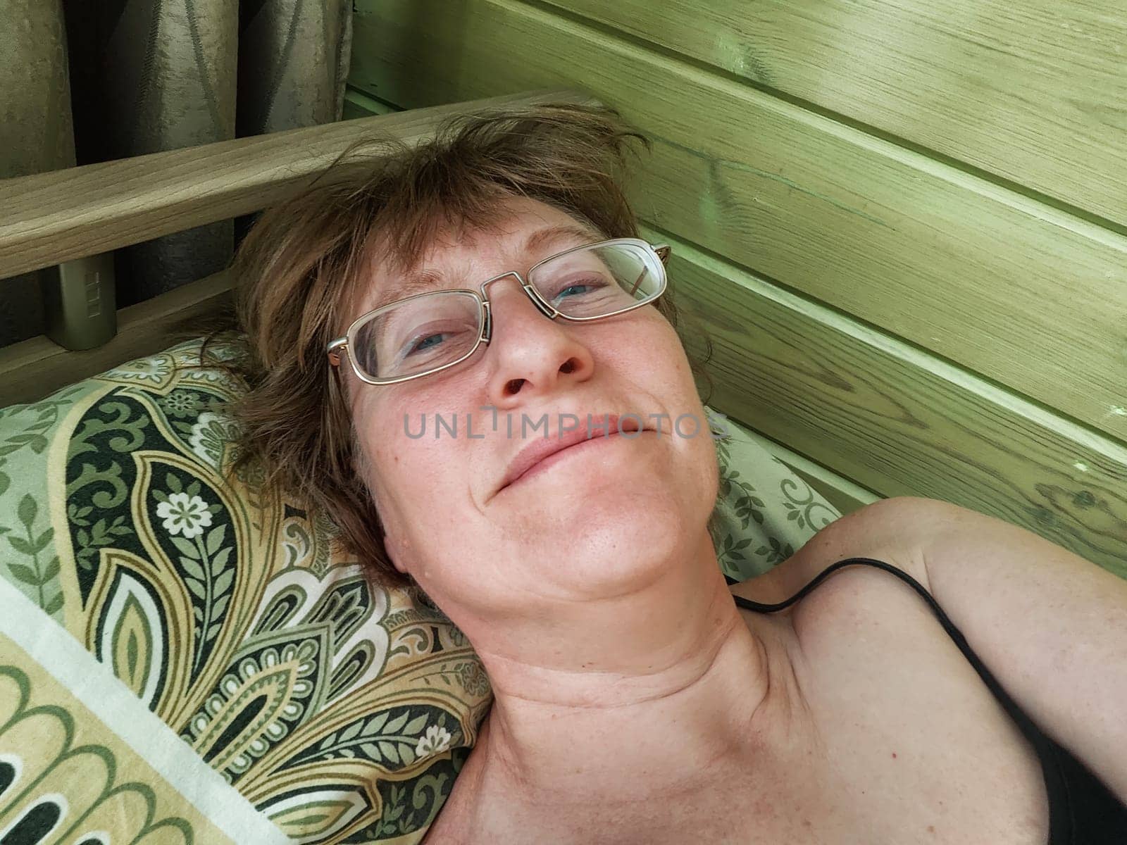 A shaggy, funny middle-aged woman in glasses takes a selfie on her smartphone in the bed in early morning. A blogger girl with disheveled hair takes pictures of herself for a blog. Daily routine by keleny