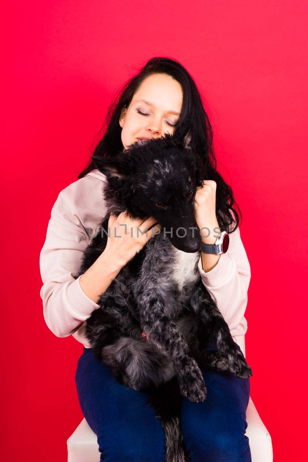 Happy lady in a casual wear hugging purebred pet dog, mudi with owner over studio background.