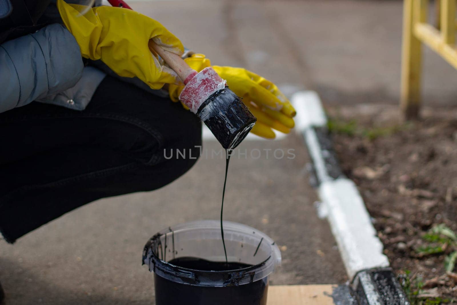 Painting with black paint. Paint on a molar brush. The work of a painter. Creation of markings on curbs. A layer of black paint on the nap of the brush.