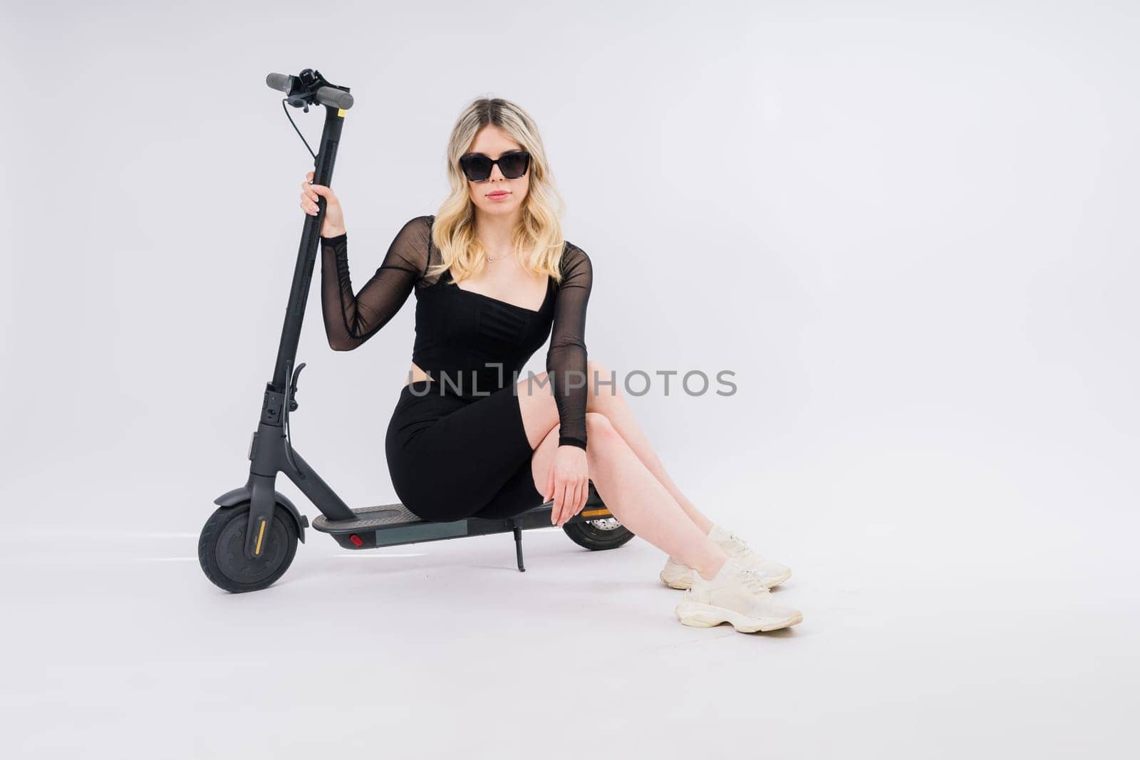 Beautiful emotional young female in a sport clothes on electric scooter on red and white background