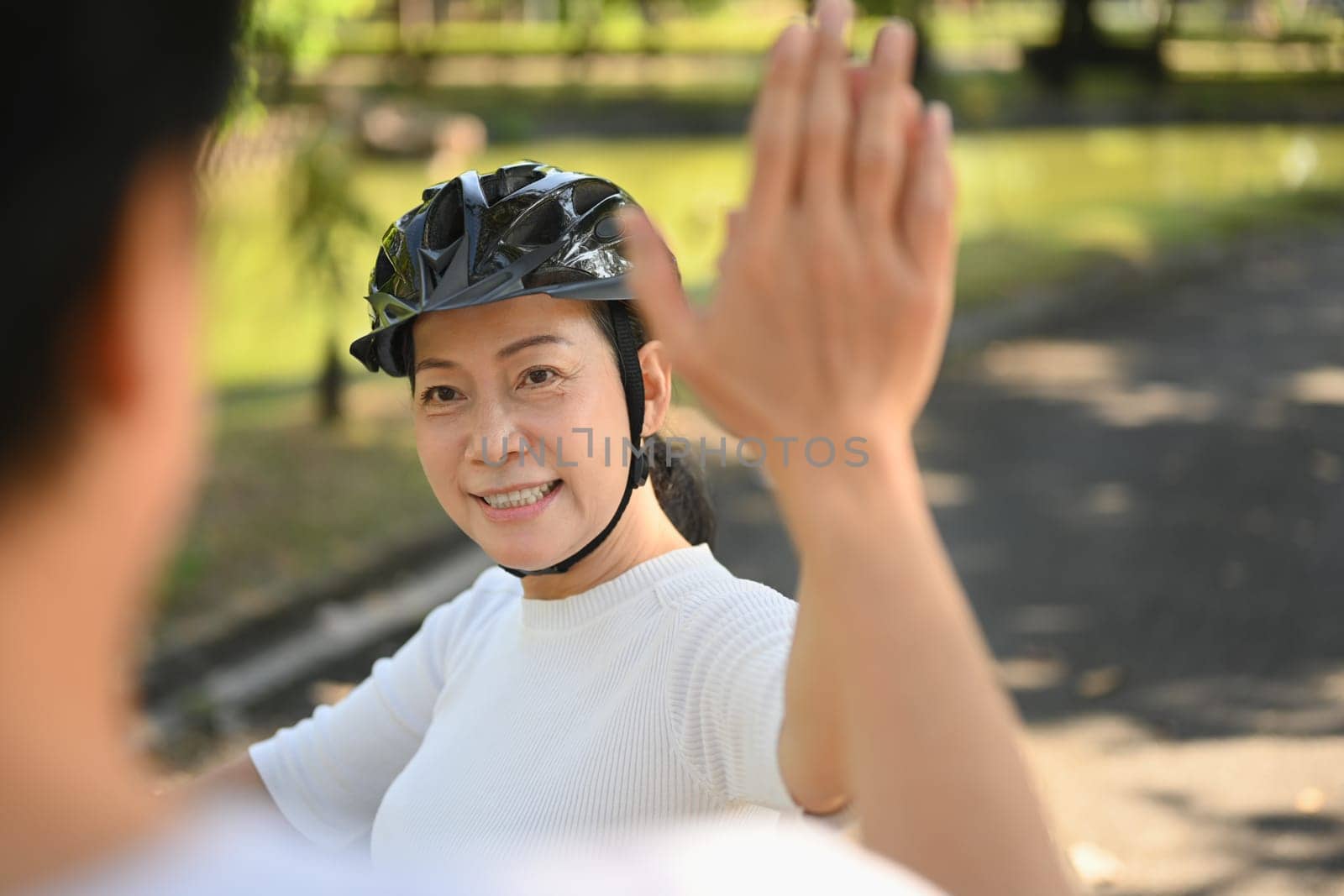Happy senior couple giving high five while riding bicycle in the park. Health care and wellbeing concept