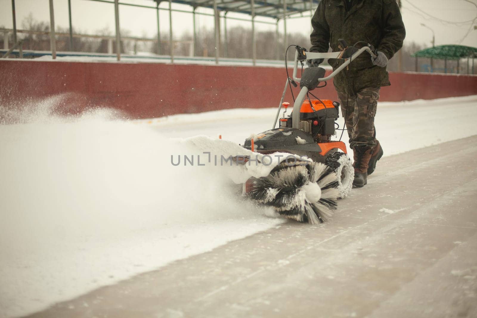 Snow removal at ice rink. Removal of layer of snow from ice. Worker cleans stadium of precipitation. by OlegKopyov