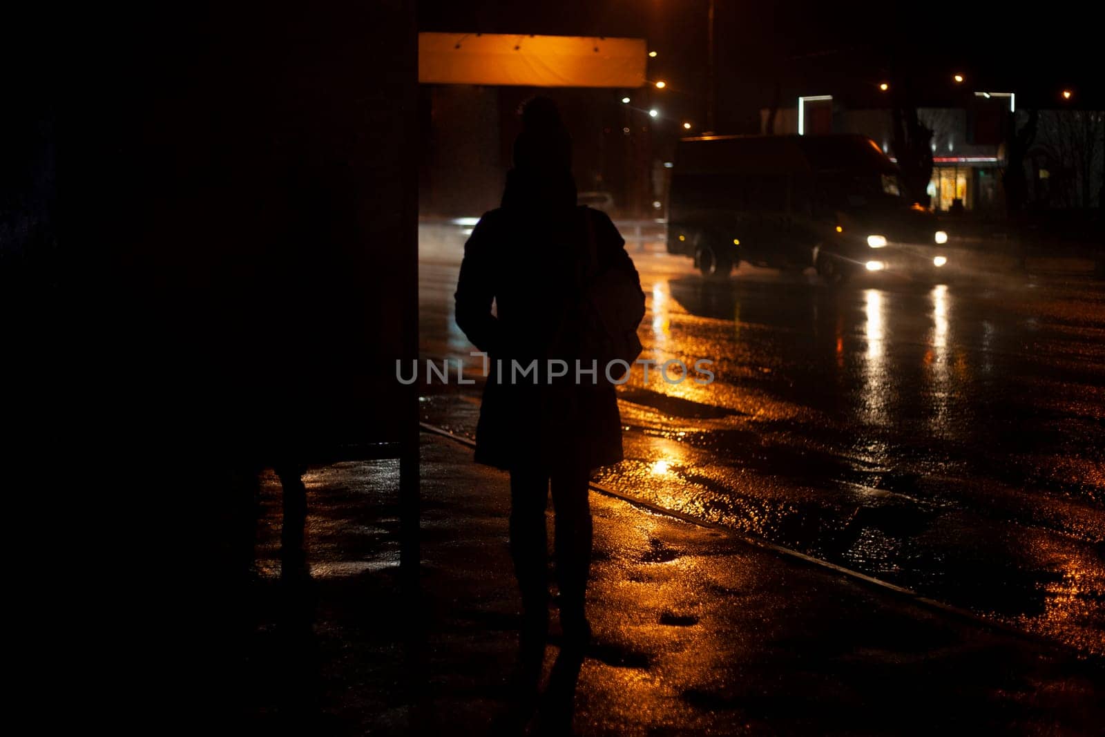 People at night in rain by road. Silhouette of man waiting for transport. Road is wet. by OlegKopyov