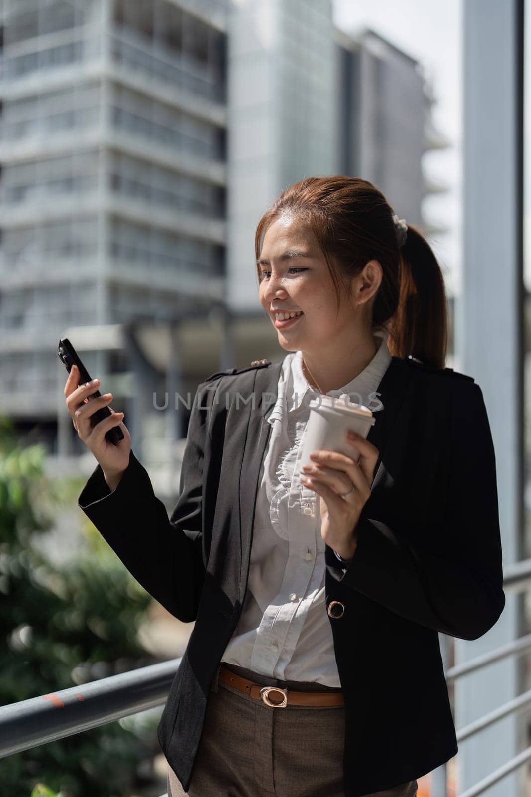 Young Asian business woman wearing suit using smartphone standing on city street outdoors by itchaznong