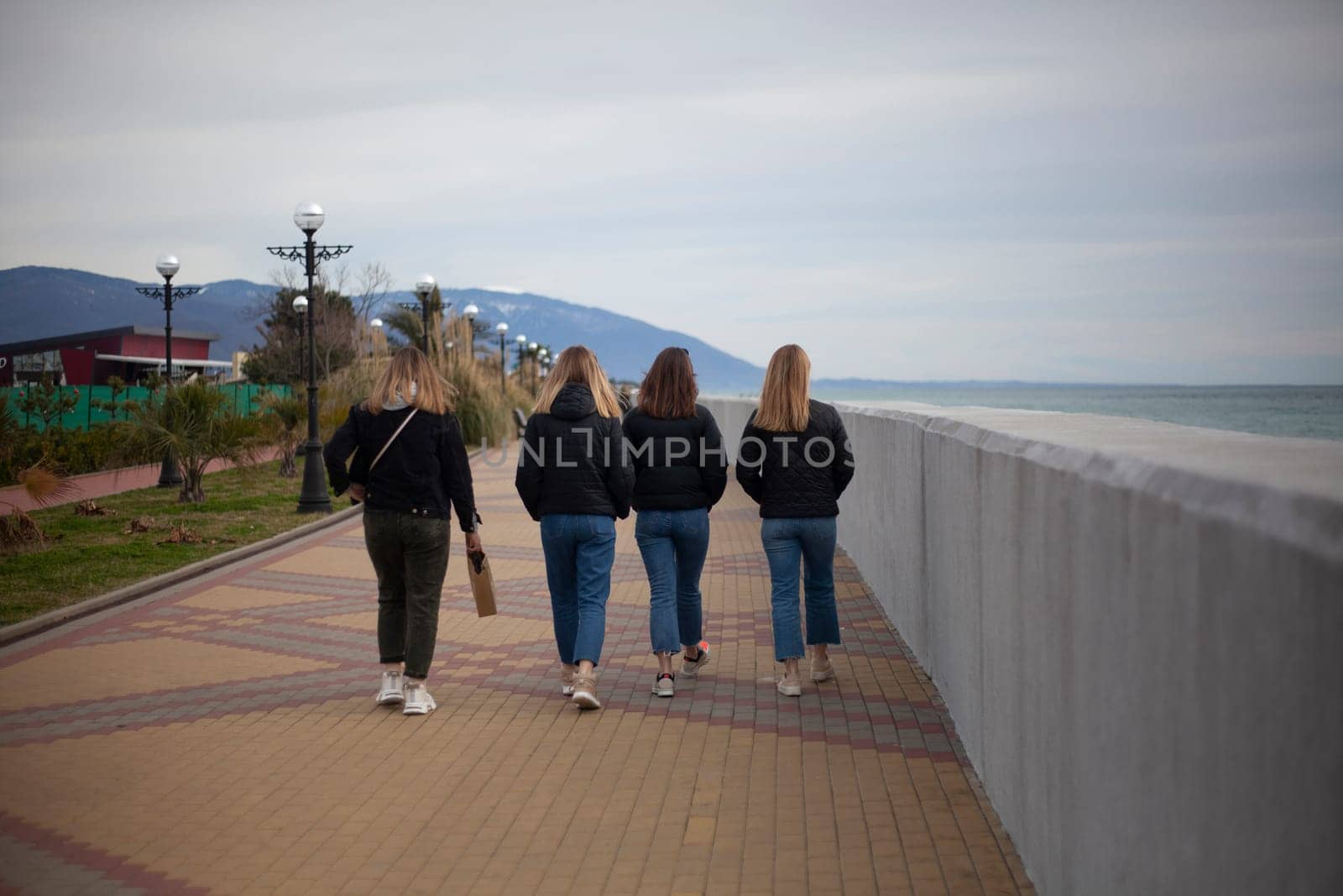 Young girls walk along the arranged promenade by the sea. Friends walk along the stone promenade. Shooting teenagers from the back. by OlegKopyov