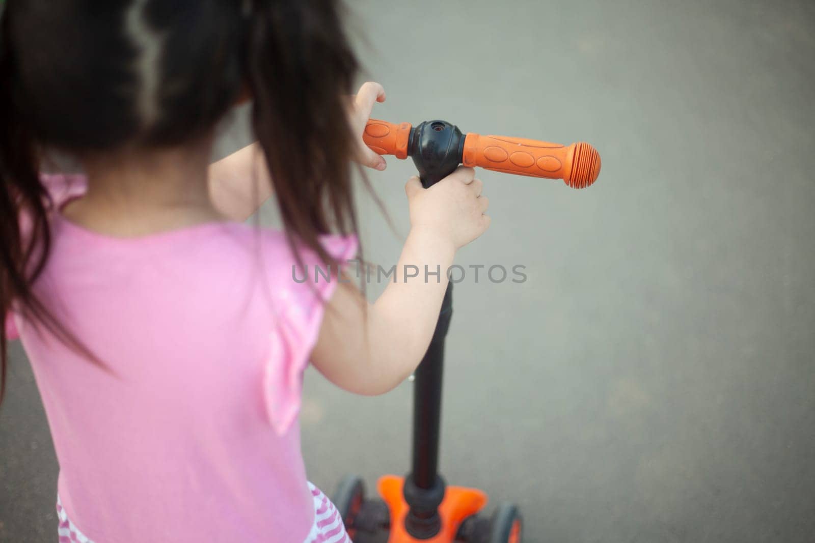 Child on scooter. Girl rides down road. Child is holding on to wheel. by OlegKopyov