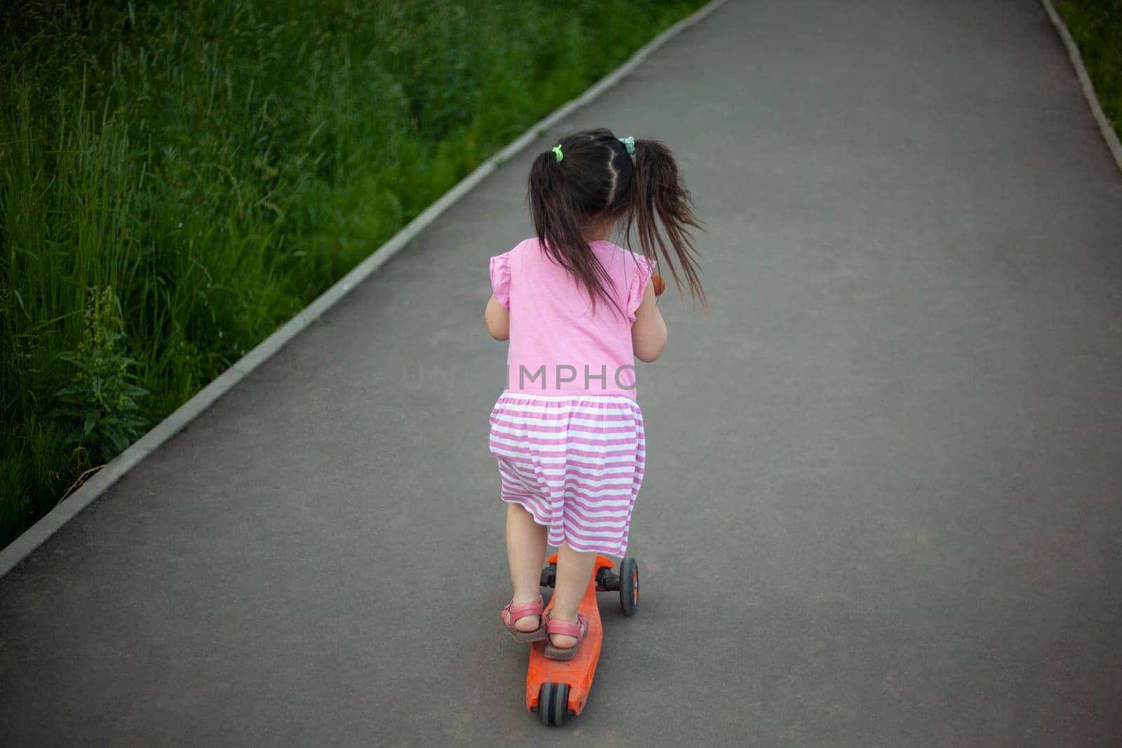 Child on scooter. Girl rides down road. Details of walk with child. by OlegKopyov