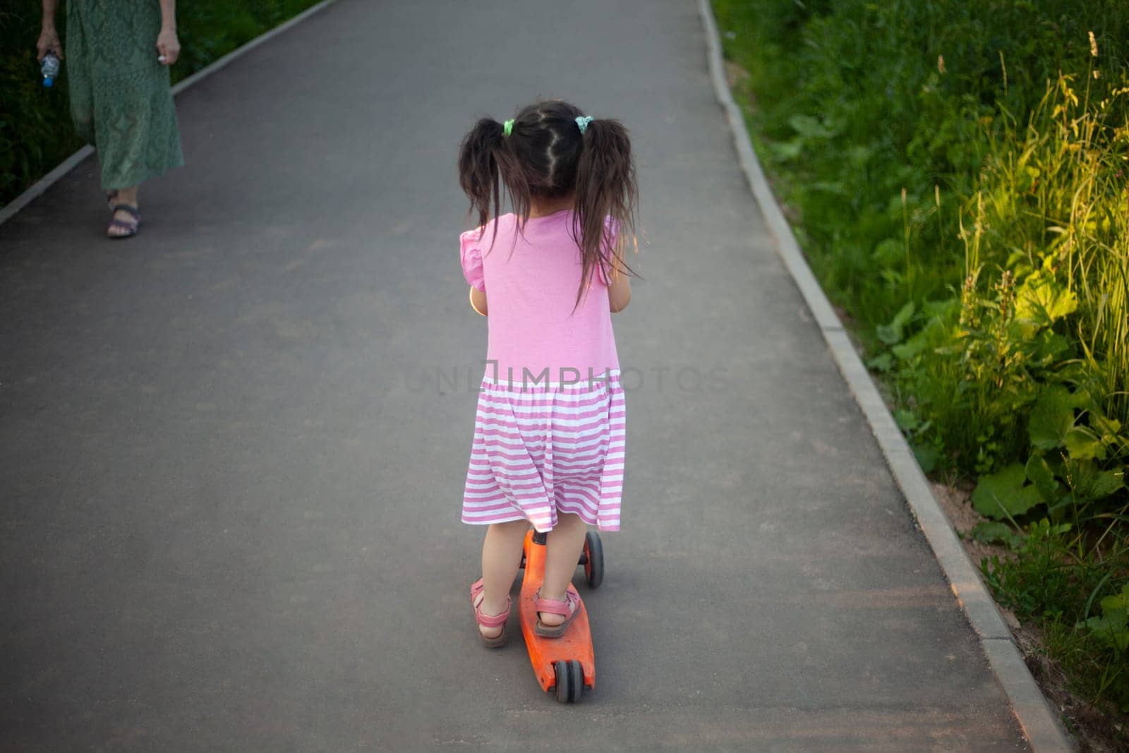 Child on scooter. Girl rides down road. Details of walk with child. by OlegKopyov