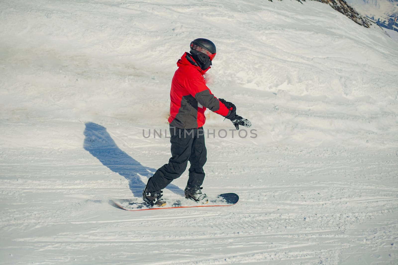 A snowboarder rides on a slope. Rest on the top of the mountain. Mountain ski resort. The guy is rolling down the mountain. Hobbies for young people.