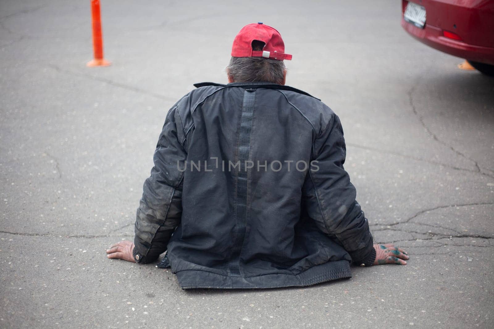 Homeless man sits on the road. A man without housing sits on the sidewalk. Man has lost the ability to walk. Poor old man is waiting for help.