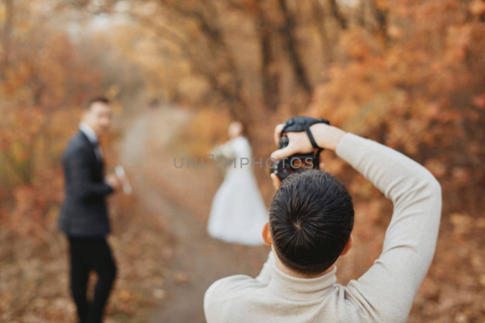 Professional wedding photographer taking pictures of the bride and groom in nature in autumn