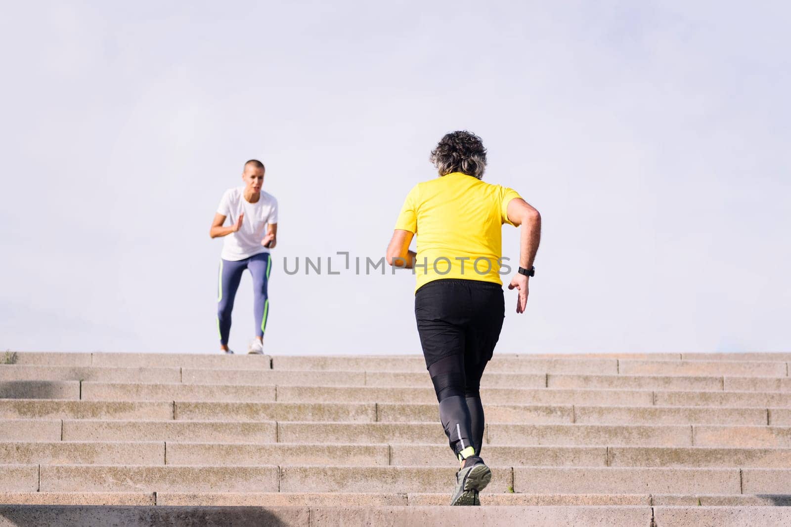 rear view of an unrecognizable sports old man training on stairs while receiving encouragement from his personal trainer, concept of active and healthy lifestyle in middle age