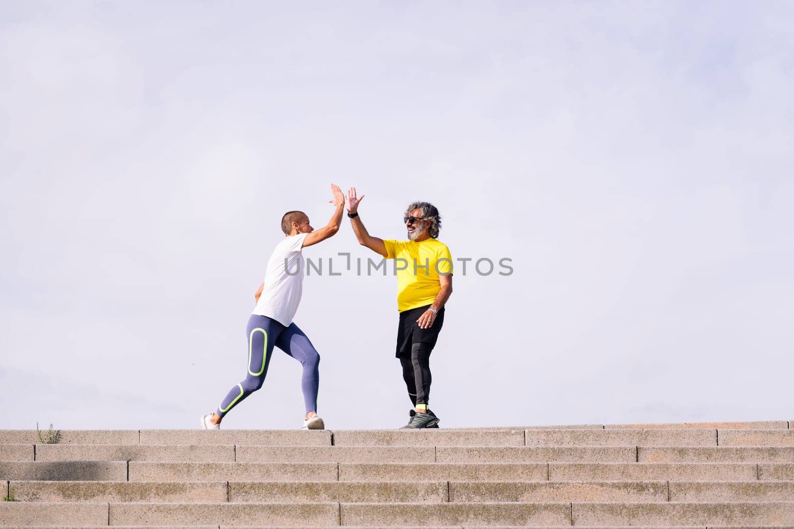 senior man celebrating the success of the effort with a high five with his personal trainer, concept of active and healthy lifestyle in middle age, copy space for text