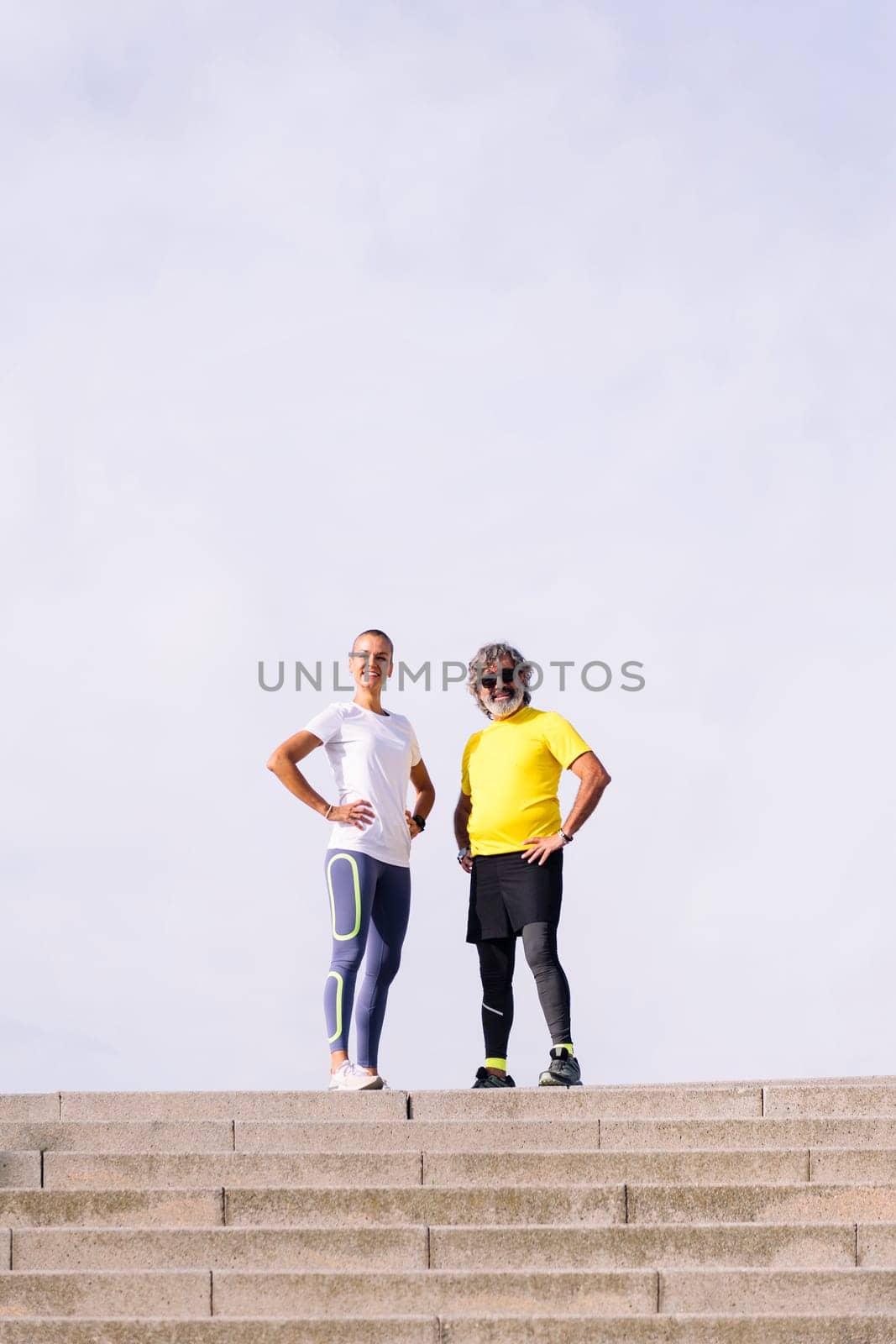 senior man and his personal trainer posing with hands on hips smiling looking at camera, concept of active and healthy lifestyle in middle age, copy space for text